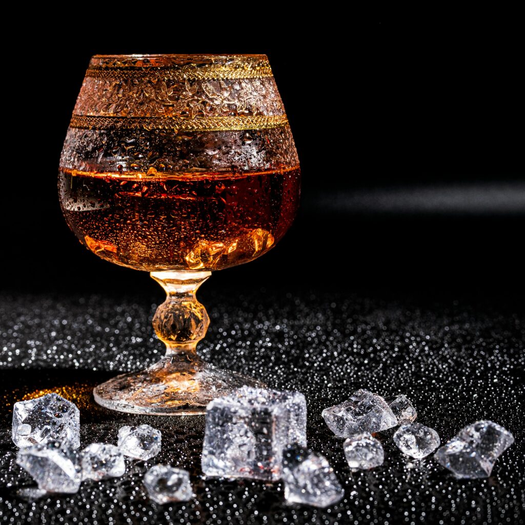 A luxurious shot of whiskey in a crystal glass surrounded by ice cubes on a textured surface.